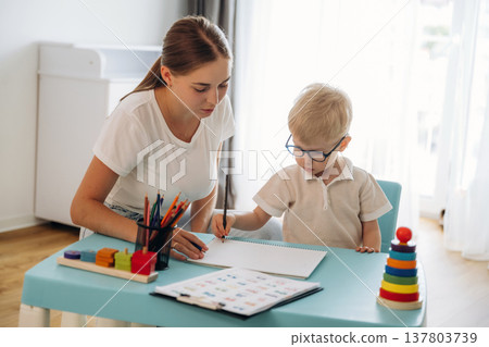Trying to learn how to draw, holding pencil. Speech therapist is with young boy indoors 137803739