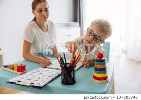 Trying to learn how to draw, holding pencil. Speech therapist is with young boy indoors Trying to learn how to draw, holding pencil. Speech therapist is with young boy indoors 137803740