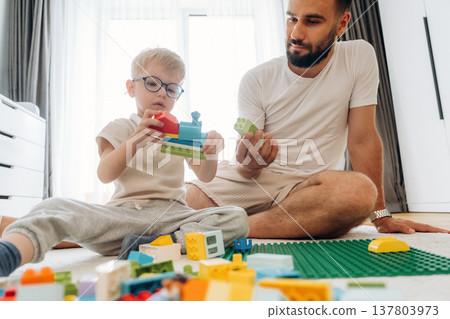 Having a great weekend. Father is playing in the room with his little son with construction sets Having a great weekend. Father is playing in the room with his little son with construction sets 137803973