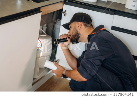 Using flashlight. Plumber working in the kitchen under the sink Using flashlight. Plumber working in the kitchen under the sink 137804141