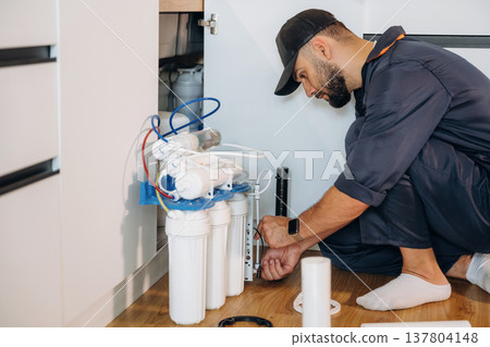 Installing new filters. Plumber working in the kitchen under the sink 137804148