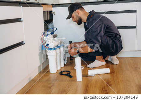 Installing new filters. Plumber working in the kitchen under the sink Installing new filters. Plumber working in the kitchen under the sink 137804149