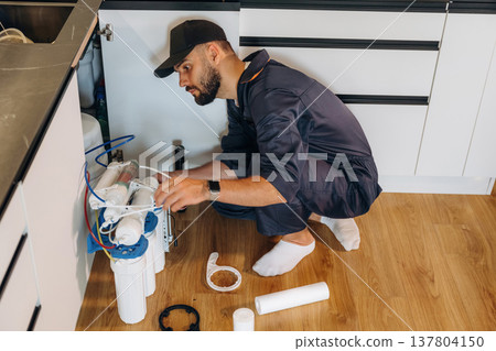 Installing new filters. Plumber working in the kitchen under the sink Installing new filters. Plumber working in the kitchen under the sink 137804150