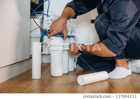 Installing new filters. Plumber working in the kitchen under the sink 137804151