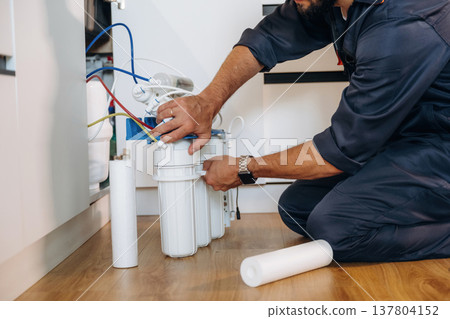 Installing new filters. Plumber working in the kitchen under the sink 137804152