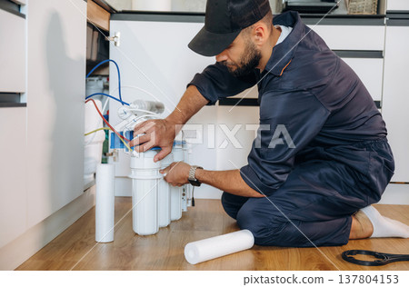 Changing filters. Plumber working in the kitchen under the sink 137804153