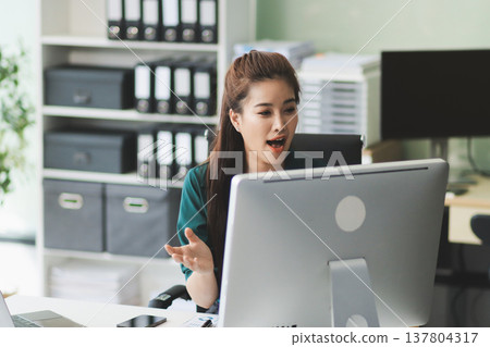Determined asian businesswoman works late in a modern office, confidently analyzing data on her laptop, embodying success and professionalism with a smile 137804317