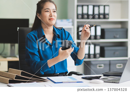 Cheerful business lady working on laptop in office, Asian happy beautiful businesswoman in formal suit work in workplace. Attractive female employee office worker smile. Cheerful business lady working on laptop in office, Asian happy beautiful businesswoman in formal suit work in workplace. Attractive female employee office worker smile. 137804328