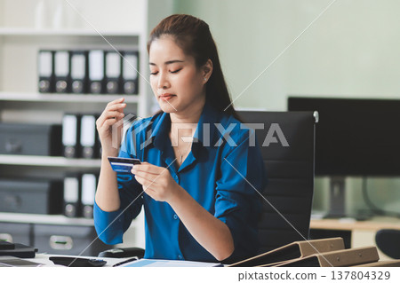 Young businesswoman is holding two credit cards with a worried expression, trying to decide which one to use to pay off her debt Young businesswoman is holding two credit cards with a worried expression, trying to decide which one to use to pay off her debt 137804329