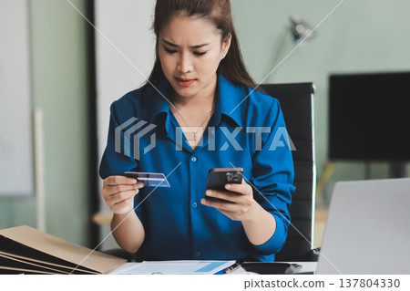 Young businesswoman is holding two credit cards with a worried expression, trying to decide which one to use to pay off her debt Young businesswoman is holding two credit cards with a worried expression, trying to decide which one to use to pay off her debt 137804330