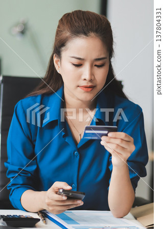 Young businesswoman is holding two credit cards with a worried expression, trying to decide which one to use to pay off her debt Young businesswoman is holding two credit cards with a worried expression, trying to decide which one to use to pay off her debt 137804331