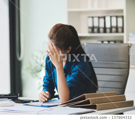 Asian businesswoman experiencing neck and shoulder pain, stretching during long hours working on computer at office 137804332