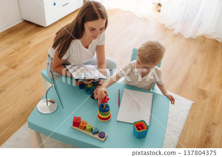 Tasks for motor skills and logic. Speech therapist is with young boy indoors Tasks for motor skills and logic. Speech therapist is with young boy indoors 137804375