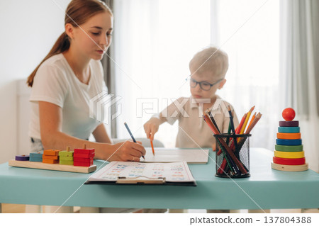 Doctor is teaching the kid. Speech therapist is with young boy indoors Doctor is teaching the kid. Speech therapist is with young boy indoors 137804388