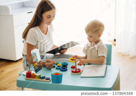 Playing with toys, motor skills. Speech therapist is with young boy indoors Playing with toys, motor skills. Speech therapist is with young boy indoors 137804389