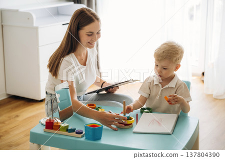 Playing with toys, motor skills. Speech therapist is with young boy indoors Playing with toys, motor skills. Speech therapist is with young boy indoors 137804390