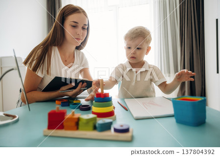 Playing with toys, motor skills. Speech therapist is with young boy indoors Playing with toys, motor skills. Speech therapist is with young boy indoors 137804392