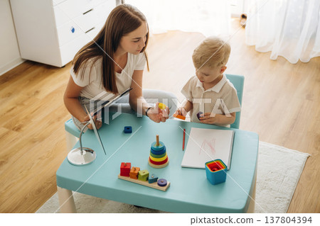 Doctor is teaching the kid. Speech therapist is with young boy indoors Doctor is teaching the kid. Speech therapist is with young boy indoors 137804394