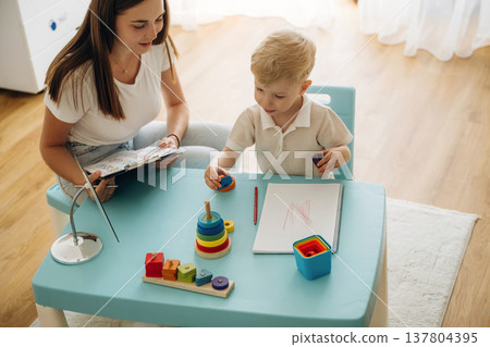 Doctor is teaching the kid. Speech therapist is with young boy indoors Doctor is teaching the kid. Speech therapist is with young boy indoors 137804395