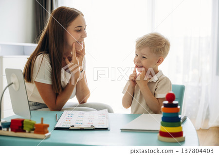 Teaches how to pronounce letters correctly. Speech therapist is with young boy indoors Teaches how to pronounce letters correctly. Speech therapist is with young boy indoors 137804403