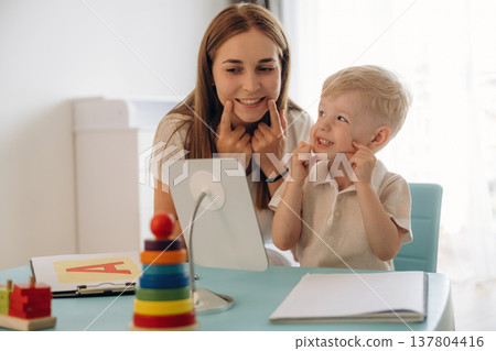 The right way to pronounce the letters. Speech therapist is with young boy indoors The right way to pronounce the letters. Speech therapist is with young boy indoors 137804416