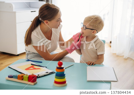 Exercises, using special device on tongue. Speech therapist is with young boy indoors 137804434