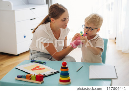 Blows into a tube with little ball. Speech therapist is with young boy indoors Blows into a tube with little ball. Speech therapist is with young boy indoors 137804441