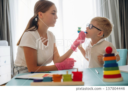 Lungs pressure force test. Speech therapist is with young boy indoors Lungs pressure force test. Speech therapist is with young boy indoors 137804446