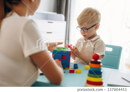 Composes logic puzzles. Speech therapist is with young boy indoors 137804451