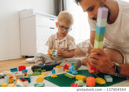 Sitting on the floor. Father is playing in the room with his little son with construction sets 137804564