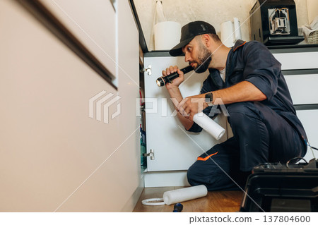 Using flashlight. Plumber working in the kitchen under the sink Using flashlight. Plumber working in the kitchen under the sink 137804600