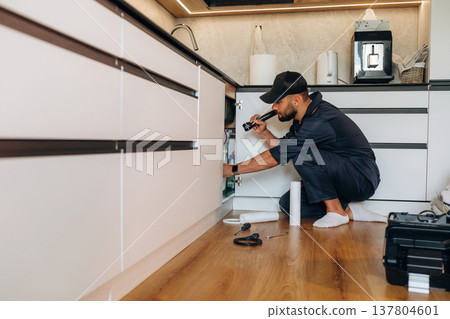 Using flashlight. Plumber working in the kitchen under the sink Using flashlight. Plumber working in the kitchen under the sink 137804601