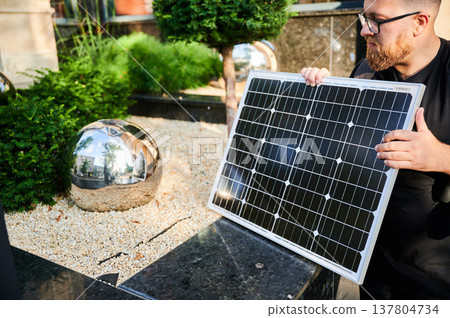 Man holding photovoltaic solar panel in front of historical building. Concept of integration of sustainable renewable energy sources into architecture. Man holding photovoltaic solar panel in front of historical building. Concept of integration of sustainable renewable energy sources into architecture. 137804734