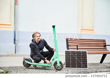 Man connects solar panel to electric scooter for charge. Integration of solar power as sustainable energy source for charging electric scooters, promoting eco-friendly urban transportation. Man connects solar panel to electric scooter for charge. Integration of solar power as sustainable energy source for charging electric scooters, promoting eco-friendly urban transportation. 137804752