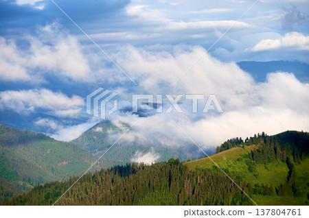 Picturesque scene of mountain valley blanketed in mist, with patches of green pastures and scattered houses. Clouds drift gently over forested hills, creating serene and tranquil atmosphere. Picturesque scene of mountain valley blanketed in mist, with patches of green pastures and scattered houses. Clouds drift gently over forested hills, creating serene and tranquil atmosphere. 137804761