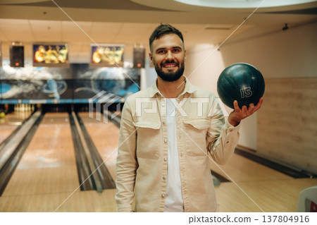 Showing the ball, standing. Man is playing bowling indoors Showing the ball, standing. Man is playing bowling indoors 137804916