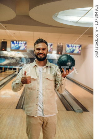 Showing the ball, standing. Man is playing bowling indoors Showing the ball, standing. Man is playing bowling indoors 137804918