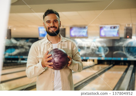 Front view, standing and holding ball. Man is playing bowling indoors 137804952
