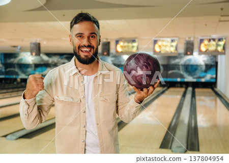 Front view, standing and holding ball. Man is playing bowling indoors 137804954