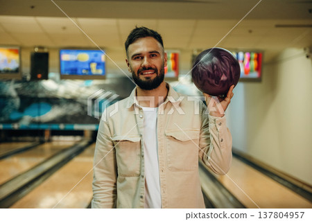 Front view, standing and holding ball. Man is playing bowling indoors 137804957