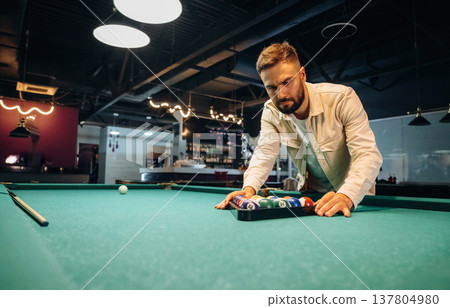 Getting ready, placing the balls. Handsome man with a pool table game 137804980