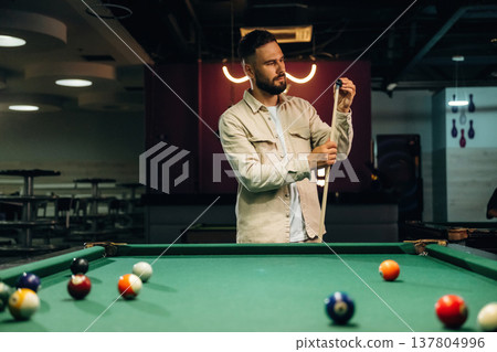 Cleaning up the top of cue stick. Handsome man with a pool table game Cleaning up the top of cue stick. Handsome man with a pool table game 137804996