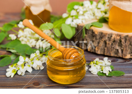 Sweet honey jar surrounded spring acacia blossoms. Honey flows from a spoon in a jar. jars of clear fresh acacia honey on wooden background 137805313