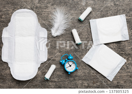 Ringing alarm clock with sanitary female tampons and menstrual sanitary pads. Medical concept of woman critical days and menstruation. Female daily hygiene. Copy space Ringing alarm clock with sanitary female tampons and menstrual sanitary pads. Medical concept of woman critical days and menstruation. Female daily hygiene. Copy space 137805325