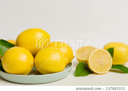Fresh cutted lemon and whole lemons over round plate on colored background. Food and drink ingredients preparing. healthy eating theme top view vith copy space Fresh cutted lemon and whole lemons over round plate on colored background. Food and drink ingredients preparing. healthy eating theme top view vith copy space 137805351