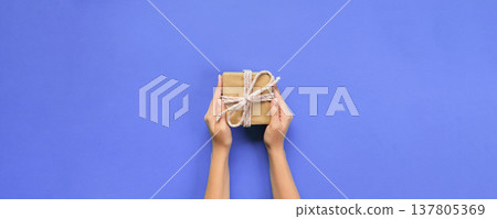 Woman hands give wrapped valentine or other holiday handmade present in paper with pink ribbon. Present box, decoration of gift on table, top view with copy space 137805369