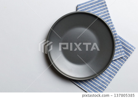 Top view on colored background empty round gray plate on tablecloth for food. Empty dish on napkin with space for your design Top view on colored background empty round gray plate on tablecloth for food. Empty dish on napkin with space for your design 137805385