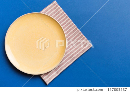 Top view on colored background empty round yellow plate on tablecloth for food. Empty dish on napkin with space for your design Top view on colored background empty round yellow plate on tablecloth for food. Empty dish on napkin with space for your design 137805387