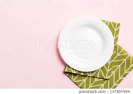 Top view on colored background empty round white plate on tablecloth for food. Empty dish on napkin with space for your design Top view on colored background empty round white plate on tablecloth for food. Empty dish on napkin with space for your design 137805404