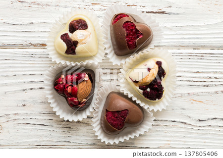 chocolate sweets in the form of a heart with fruits and nuts on a colored background. top view with space for text, holiday concept chocolate sweets in the form of a heart with fruits and nuts on a colored background. top view with space for text, holiday concept 137805406